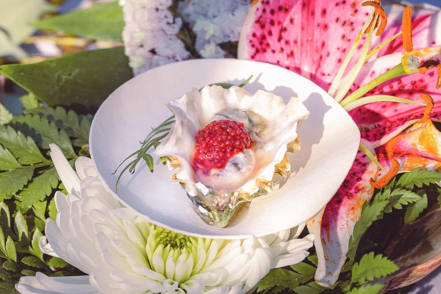 A single oyster dressed with pink sauce among lilies