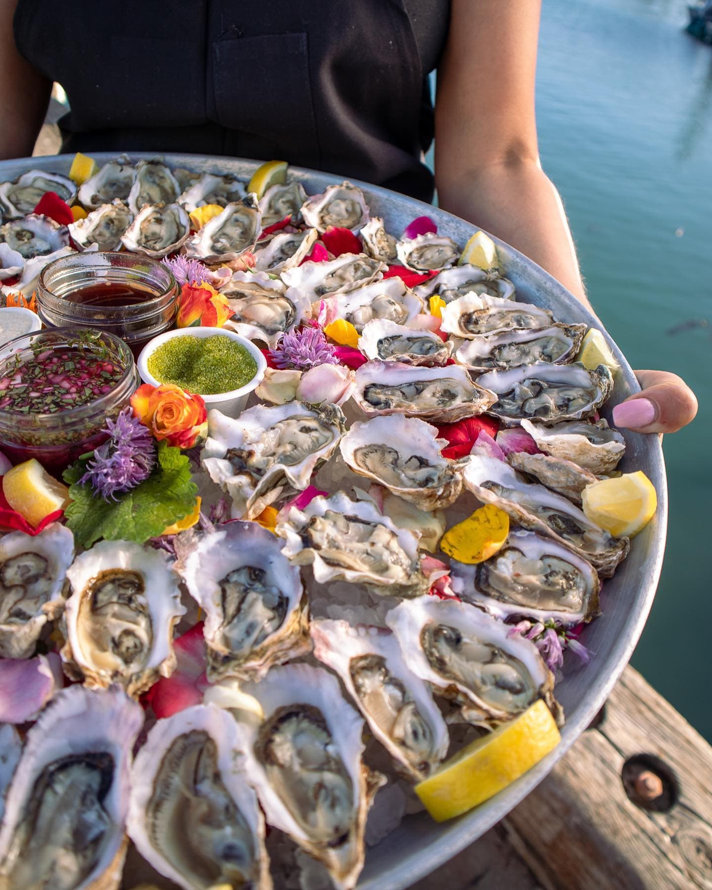 A tray of dressed oysters with lemons and herbs held over the harbor